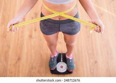 Top view of pretty slim woman with measure around her body is standing on the scales. - Powered by Shutterstock