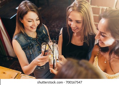 Top view of pretty smiling female friends clinking glasses of cocktails at bar