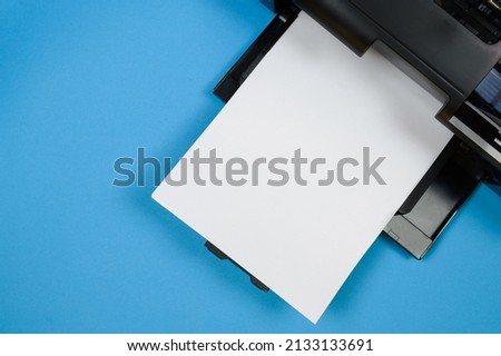 Top view of the printer and a blank sheet of a4 paper on a blue background
