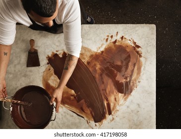 Top view professional black baker uses hot chocolate to draw lovely heart  before making sweet organic bars as romantic gifts for valentine day  Isolated marble table in artisan retro laboratory