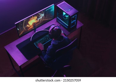 Top view of professional cyber sportsman in headphones playing shooter video game on his powerful gaming PC in dark neon room at night. Pro gamer participates in online esport tournament. Cyber sport - Shutterstock ID 2150257059