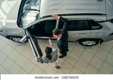 Top View Of Professional Salesperson During Work With Customer At Car Dealership. Successful Young Businessman In A Suit Chooses A New Car.