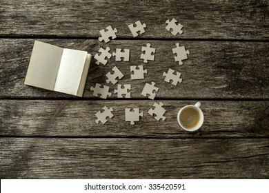 Top view of puzzle pieces scattered on a rustic wooden study desk with cup of coffee and open notepad alongside. Conceptual of education, science and solution to a problem or question. - Powered by Shutterstock