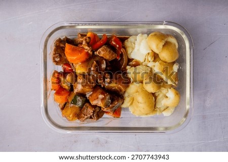 A top view of a pyrex of mixed beef, colorful vegetables in cubes with sauce served with boiled potatoes on a white background