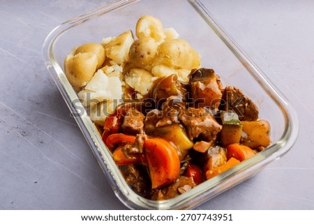 A top view of a pyrex with mixed beef, colorful vegetables in cubes and sauce served with boiled potatoes on a white background