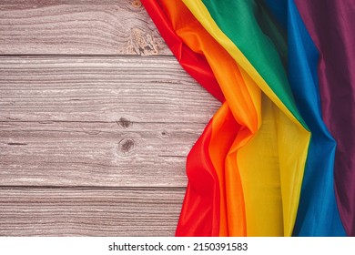 Top View Of The Rainbow Flag Or LGBT Over A Wooden Table With Copy Space For Text. Flat Lay