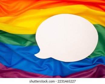 Top view of rainbow flag or LGBT flag with a blank white speech bubble. Close-up photo. Space for text. Gender diversity concept - Shutterstock ID 2231465227