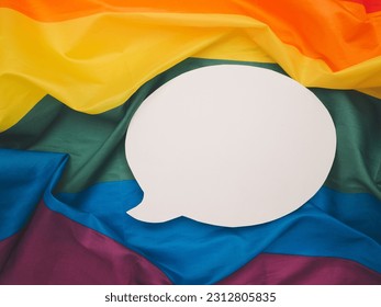 Top view of rainbow flag or LGBT flag with a blank white speech bubble. Close-up photo. Space for text. Gender diversity concept