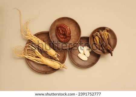 Top view of rare herbal displayed on wooden dishes - ginseng roots, ganoderma mushrooms and red ginseng. Beige background for advertising product and space for design