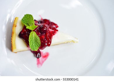 Top view of raspberry cheesecake with fresh cherry on white plate.