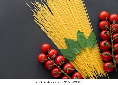 Top View Of Raw Spaghetti Near Cheery Tomatoes And Basil On Black Background