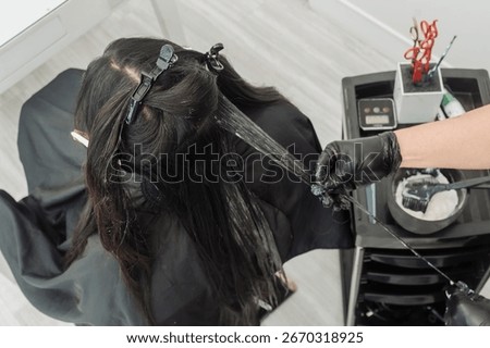 Top view of the rebonding procedure in progress. A stylist carefully applies rebonding cream to a thin strand of hair using precision techniques while other sections are clipped.