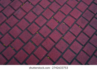 Top view of red diamond pattern paving blocks texture with scattered small yellow leaves. Urban sidewalk background