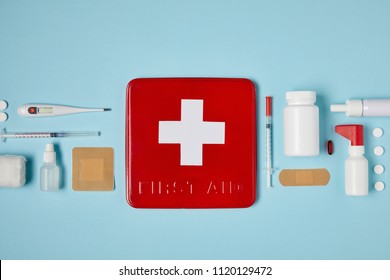 top view of red first aid kit box on blue surface with medical supplies