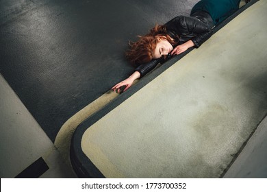 Top View Of Red Haired Girl Laying On Floor Inside Parking House Along Curb. Young Woman With Closed Eyes Sleeping Or Acting Dead Victim Of Accident. Image.