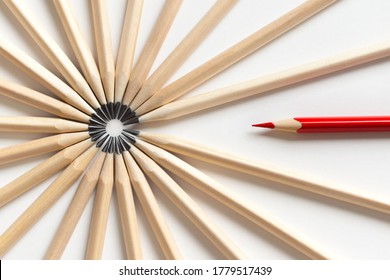 Top View Of A Red Pencil Tends To Fall Into A Circle Of Gray Pencils Lying On A White Background. Concept Of Unsuitable Standout Employee In An Office Team. Eccentric Concept