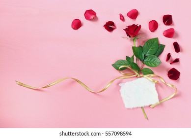 Top view of red rose with empty greeting card on pastel pink background