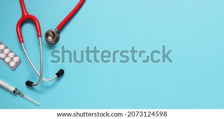 Top view of red stetoscope, syringe and white pills on blue background. Medicine concept.
