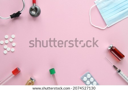Top view of red stetoscope, syringe, mask, ampoules and white pills on pink background. Medicine concept.