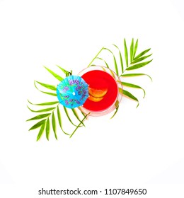 Top View Of Red Summer Cocktail Decorated With Umbrella On A White Background With With Palm Tree Leaves. Copy Space.