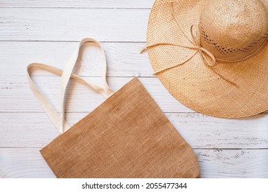 Top View Of Reusable Sackcloth Bag With White Holder And Brown Floppy Lady Straw Hat With Raffia Straw Ribbon On White Wooden Background , Easy Holiday Concept