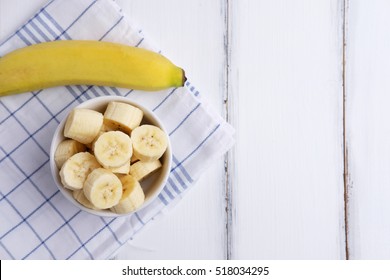 Top View Of Ripe Yellow Banana Slice In Cup On White Wood Background, Blank Space And Selective Focus.