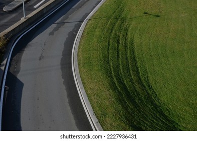 top view of the road. the slope and the surrounding area of the road is an exemplary mowed lawn with stripes. metal barrier around road I will sit in the commanded direction and arrow. approach turn