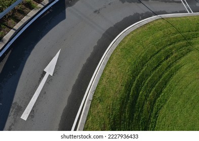 top view of the road. the slope and the surrounding area of the road is an exemplary mowed lawn with stripes. metal barrier around road I will sit in the commanded direction and arrow. approach turn
