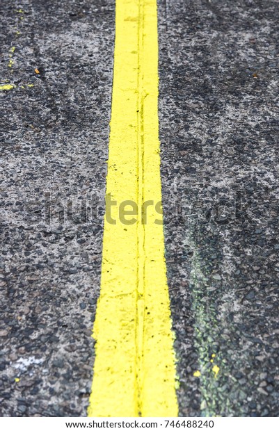 Top view of\
road with yellow line in middle, vertical.\
High angle view of grey\
asphalt road with a yellow\
line.\

