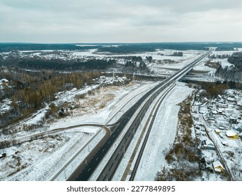 Top view of the roadway in winter. Snow-covered road and roadside. The highway passes through the forest and the private sector. Detailed photos from the drone of the road infrastructure. - Powered by Shutterstock