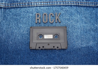 Top View Of ROCK Black Lettering Word With An Old Black Cassette Over A Jean Jacket. Fashion And Music Concept