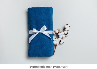 Top view of rolled up blue towel with cotton twig on gray background with copy space.
