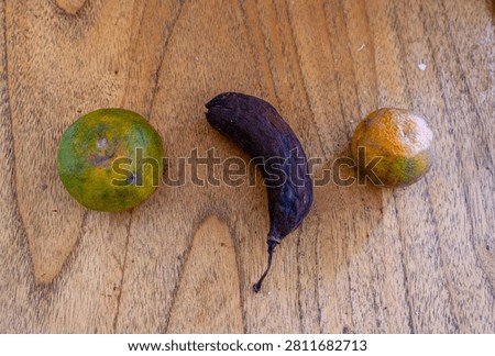 A top view of rotting fruit, including rotting bananas and moldy oranges, is displayed on a wooden table. This image illustrates food waste, fruit spoilage, improper food storage, spoilage, and expired products.