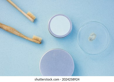 Top View Of Round Silver Cans, Bamboo Toothbrushes, Glass Cup With Tooth Paste Smudge On Pastel Blue Background. Zero Waste Hygiene Accessories Concept.