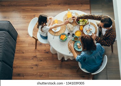 Top View Of The Round Table And Parents Having Breakfast With Their Daughter