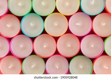 Top view of rows of unused multicolored wax tea light candles. Row of new water candles as background. A lot of candles on pink background, close-up. 