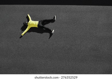 Top view runner in yellow sportswear resting lying on a black asphalt after running. Jogging man taking a break during training outdoors. Caucasian fitness model 20s in Barcelona, Spain. 