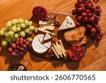 Top view of a rustic cheese platter with grapes, toast, pomegranate, and assorted cheese on a wooden board. Perfect setup for a wine and cheese evening.