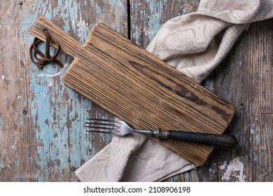 Top view of rustic cutting board, fork and folded linen serviette on blue grunge and shabby wooden background