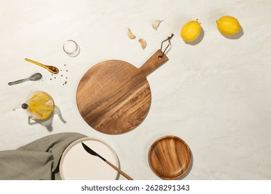 Top view of a rustic kitchen scene with round wooden board, garlic, lemons, olive oil, and utensils on a light marble background. Ideal for culinary, recipe, and home cooking concepts.