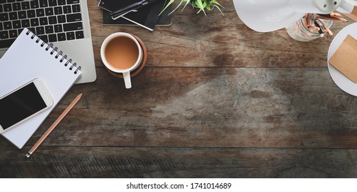 Top view of rustic table office desk with coffee cup putting surrounded computer laptop, note, pencils, pencil holder, potted plant , lamp, pen and smartphone. - Powered by Shutterstock