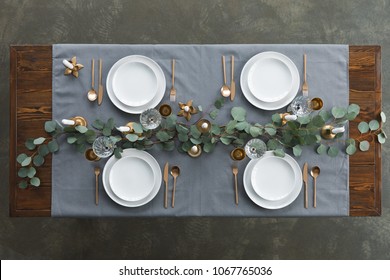 top view of rustic table setting with eucalyptus, tarnished cutlery, wine glasses, candles and empty plates on tabletop
