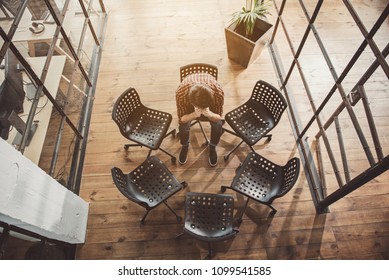 Top View Sad Man Closing Face By Hands While Locating Alone In Office. Melancholy Concept