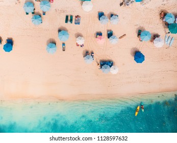Top view of sandy beach with turquoise sea water and colorful blue umbrellas, aerial drone shot