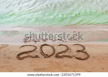 Top view of the sandy shore on which the numbers of the outgoing year 2022 are drawn, which were almost washed away by a wave of green water, and the clear numbers of 2023 of the new coming year.