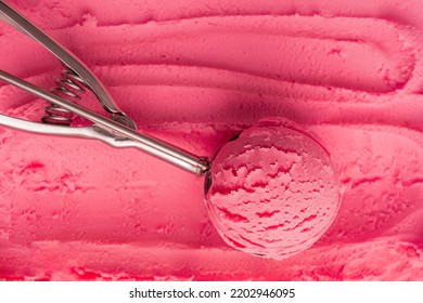 Top view of scoop of pink cold sweet ice cream or sorbet made with juicy red berries, raspberry or strawberry in metal silver serving spoon on textured gelato background. Refreshing natural dessert