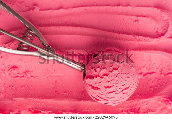 Top view of scoop of pink cold sweet ice cream or\
sorbet made with juicy red berries, raspberry or strawberry in\
metal silver serving spoon on textured gelato background.\
Refreshing natural dessert