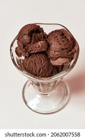 Top View Of Scoops Of Tasty Chocolate Ice Cream In A Glass Sundae Dish Isolated Over Light Background. Sweet Junk Food Concept. Vertical Shot