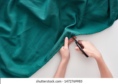 top view of seamstress cutting colorful fabric with scissors on white background 