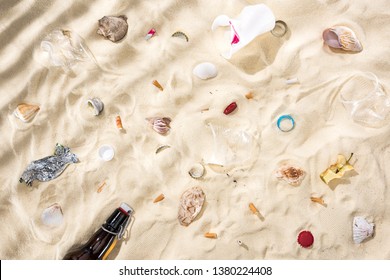 Top View Of Seashells, Scattered Cigarette Butts, Apple Core, Plastic Cups, Glass Bottle And Candy Wrapper On Sand